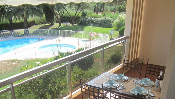 A balcony with a dining table set for four, overlooking a swimming pool and lush greenery. - Luxury apartment with stunning views 150 meters of beach. (Cavalaire-Sur-Mer)