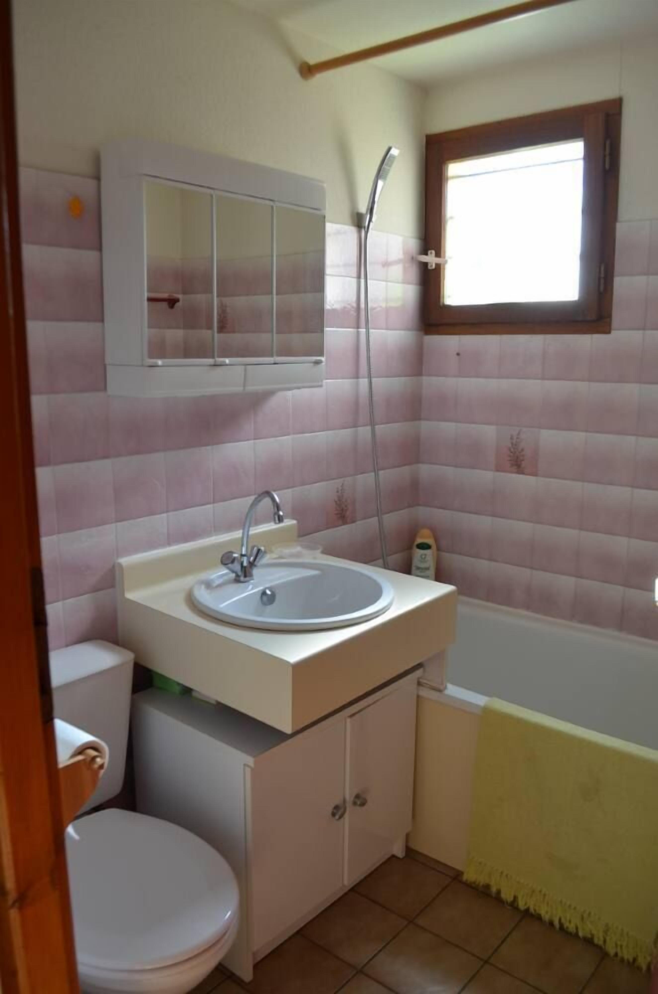 Une petite salle de bain comprenant un lavabo, des toilettes et une fenêtre située au-dessus de la baignoire.