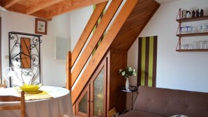 Un salon chaleureux avec un plafond en bois, une table à manger avec des chaises, un canapé marron et une étagère contenant des ustensiles de cuisine.