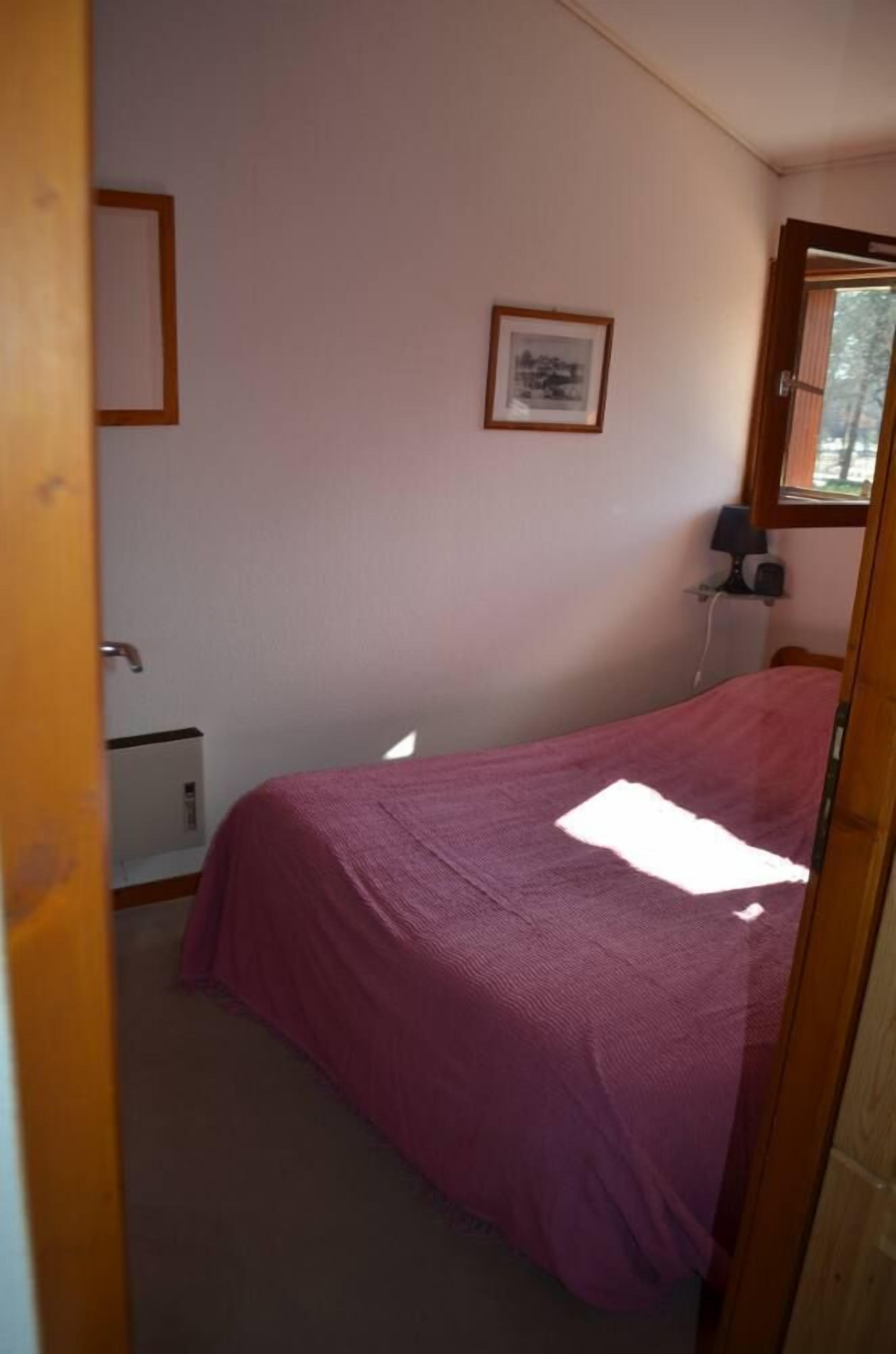 Une chambre à coucher avec un lit, un tableau encadré au mur, un bureau avec une lampe et une fenêtre.