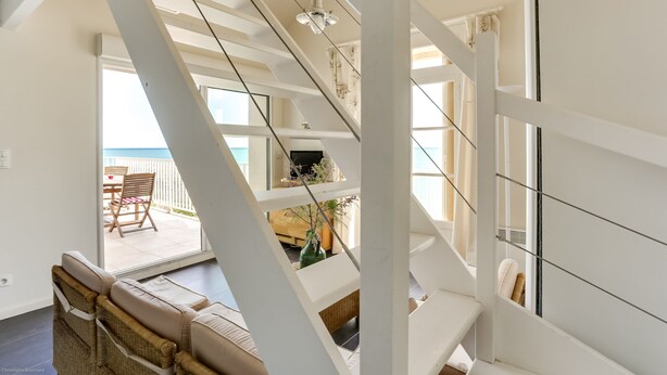 Un intérieur moderne avec un escalier menant à un balcon d’où l’on a vue sur la mer.