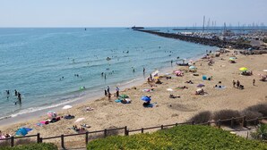 Une plage où l’on peut se baigner et bronzer, une jetée avec des bateaux, et un ciel dégagé.
