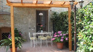 Un patio al aire libre con una pérgola de madera, una mesa con sillas y plantas en macetas.