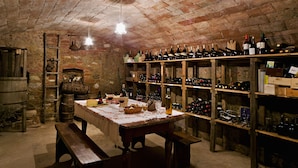Una bodega con estantes de madera llenos de botellas de vino, una mesa con copas y una botella, y un banco de madera.