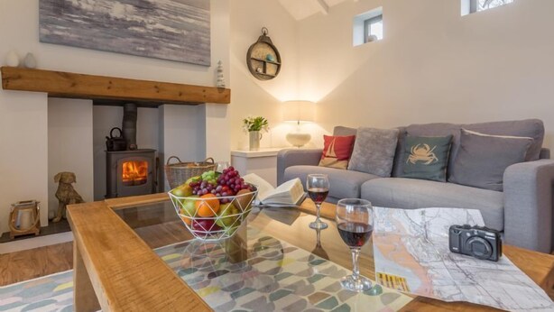 Una sala de estar acogedora con chimenea, un sofá, una mesa de centro con frutero, copas de vino y una cámara.