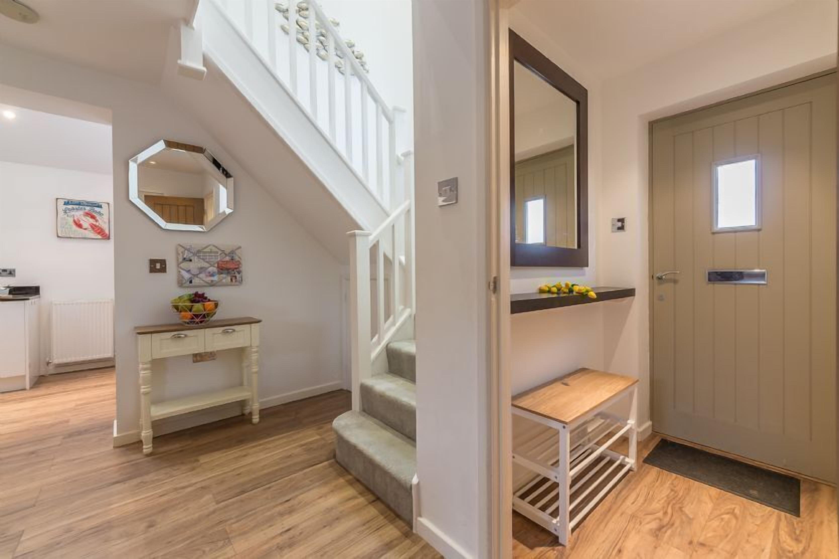 A modern interior with a staircase, a white console table with a fruit bowl, a mirror, and a wooden door.