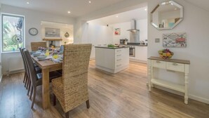 Una cocina moderna con armarios blancos, una isla central y un comedor con sillas de mimbre y una mesa de madera.