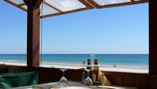 A table set for dining with a view of the beach and ocean.
