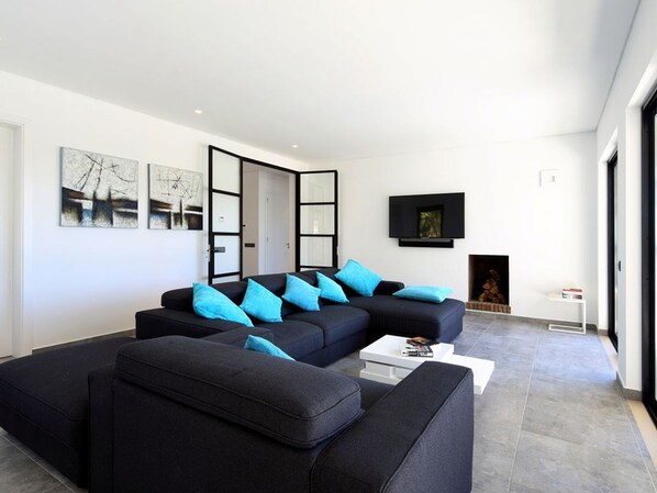 A modern living room with a sectional sofa, a flat-screen TV, and a fireplace.