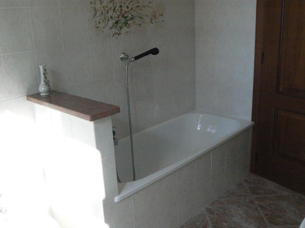 A bathroom with a bathtub, a shower, and a small shelf with a vase.