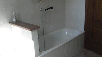 A bathroom with a bathtub, a shower, and a small shelf with a vase.