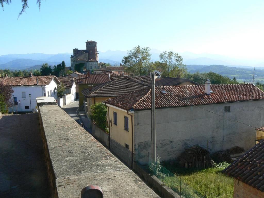 A narrow street with traditional buildings, a church tower, and a clear view of distant mountains.