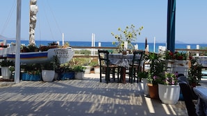 Une terrasse avec une table et des chaises, des plantes en pot et une vue sur la mer.