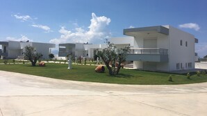 Un complexe résidentiel moderne composé de plusieurs bâtiments blancs, avec une pelouse bien entretenue et un ciel d’un bleu éclatant.
