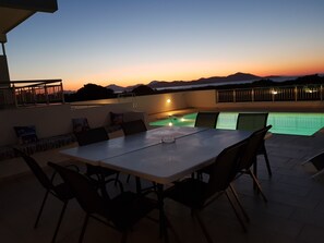 Een terras buiten met een zwembad, een eettafel en stoelen.
