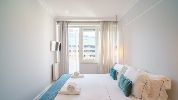 Hotellihuone, jossa on suuri sänky, seinälle asennettu televisio ja ikkuna, jossa on verhot.