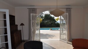 An open living area with a view of a swimming pool, a black armchair, an orange armchair, and a wooden cabinet. - Quiet Villa in Private Domain, Seaview, Heated Pool, BBQ, Walk to the Beach (Roquebrune-Sur-Argens)