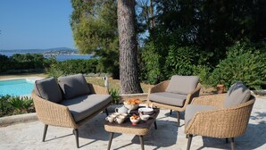 A wicker outdoor seating area with a table set for breakfast, overlooking a pool and a scenic view. - Quiet Villa in Private Domain, Seaview, Heated Pool, BBQ, Walk to the Beach (Roquebrune-Sur-Argens)