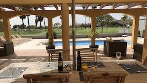 Un patio exterior con mobiliario de madera, piscina y vistas a un campo de golf.