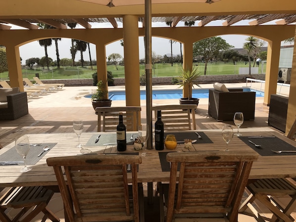 Une terrasse extérieure avec des meubles en bois, une piscine et une vue sur un terrain de golf.