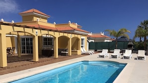 Una piscina con sillas de descanso y un área de patio techada.