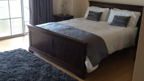 A bedroom with a large bed, a nightstand, a dark rug, and a window with curtains.