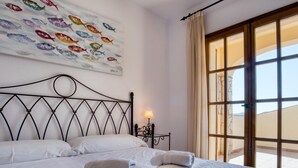 A hotel room with a bed, a nightstand, a lamp, a window with curtains, and a wall art piece.