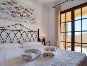 A hotel room with a bed, a nightstand, a lamp, a window with curtains, and a wall art piece.
