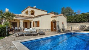 A two-story house with a swimming pool, outdoor seating, and stone walls.