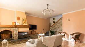 A living room with a stone fireplace, a sofa, wicker chairs, and a staircase leading to another level. - Il Poggiolo, house between country and sea! (Montemagno)