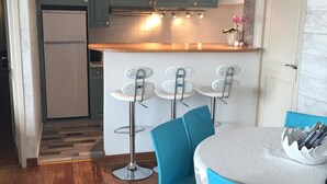 Una cucina compatta con mobili color petrolio, un frigorifero bianco e un piano di lavoro in legno. Sono presenti tre sgabelli da bar e un tavolo rotondo con sedie.