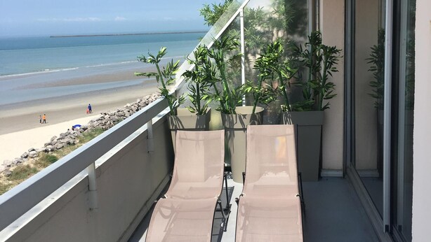 Un balcone con due poltrone, vista sulla spiaggia e piante in vaso.