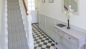 A staircase with a checkered floor, a white console table with a vase, and a mirror on the wall.