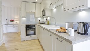 A modern kitchen with white cabinetry, a built-in oven, a sink, and a countertop with a toaster, kettle, and croissant.