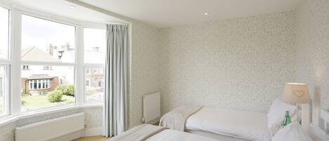 A bedroom with two beds, a window with curtains, a radiator, and a lamp with a heart design.