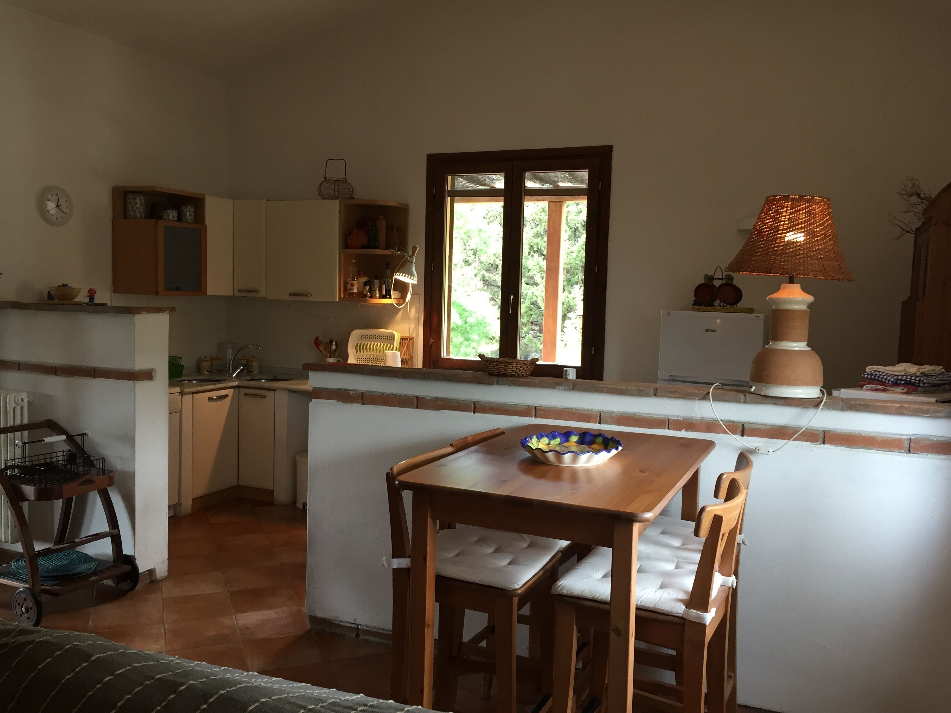 Una cucina compatta con zona pranzo, una finestra vista su del verde e una lampada sul piano di lavoro.