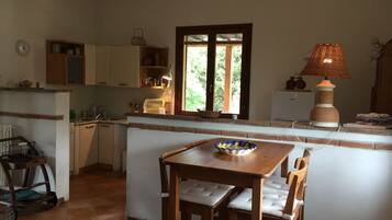 Una cucina compatta con zona pranzo, una finestra vista su del verde e una lampada sul piano di lavoro.