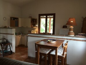 A compact kitchen with a dining area, a window with a view of greenery, and a lamp on the countertop.