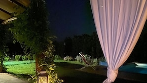 Un espacio de patio al aire libre con un farol, tela blanca drapeada y una piscina al fondo.