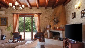 A cozy living room with a fireplace, wooden ceiling beams, and a large TV. - Stone Made villa in picturesque village! Private pool & full privacy! (Rethymno)