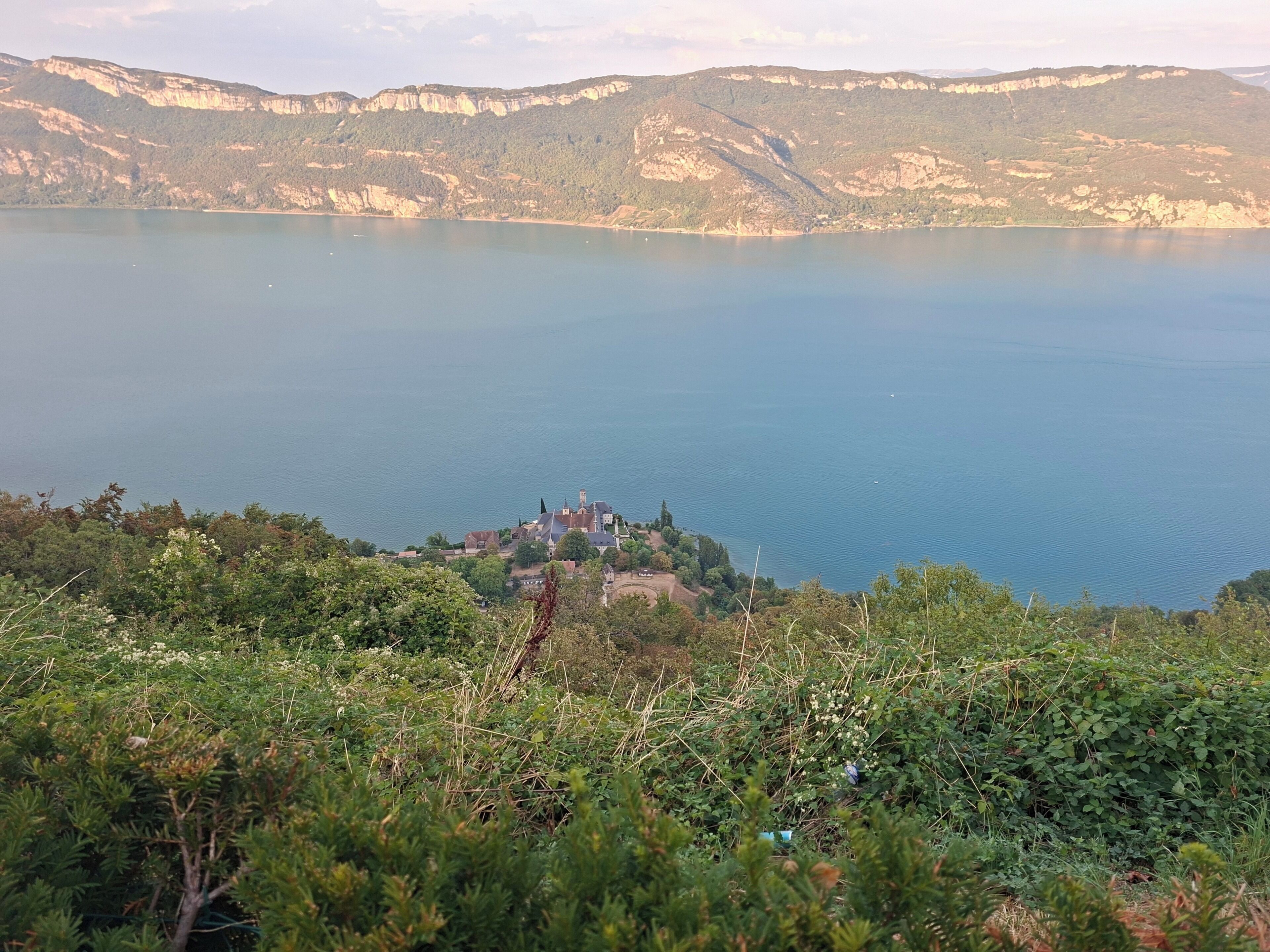 Un paisaje costero con una masa de agua, un pequeño poblado con edificios y un fondo montañoso.