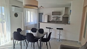 Une cuisine moderne dotée d’un four et d’un micro-ondes encastrés, un coin repas avec une table en verre et des chaises noires, et un salon avec un canapé.