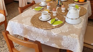 Una mesa de comedor preparada con alimentos para el desayuno, un aparador con puertas de vidrio y un televisor sobre un tocador de madera.
