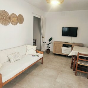 Una sala de estar con un sofá, un televisor, una mesa de comedor y una planta.