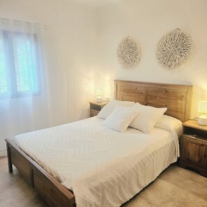 A neatly made bed with a wooden headboard, two wall-mounted decorative items, and a bedside table with a lamp.
