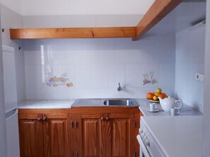 Une cuisine avec des meubles de rangement en bois, un plan de travail blanc, un évier et une cuisinière.