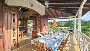 Un espacio de comedor al aire libre cubierto con una mesa lista para dos, sillas de madera y vistas a un paisaje exuberante.