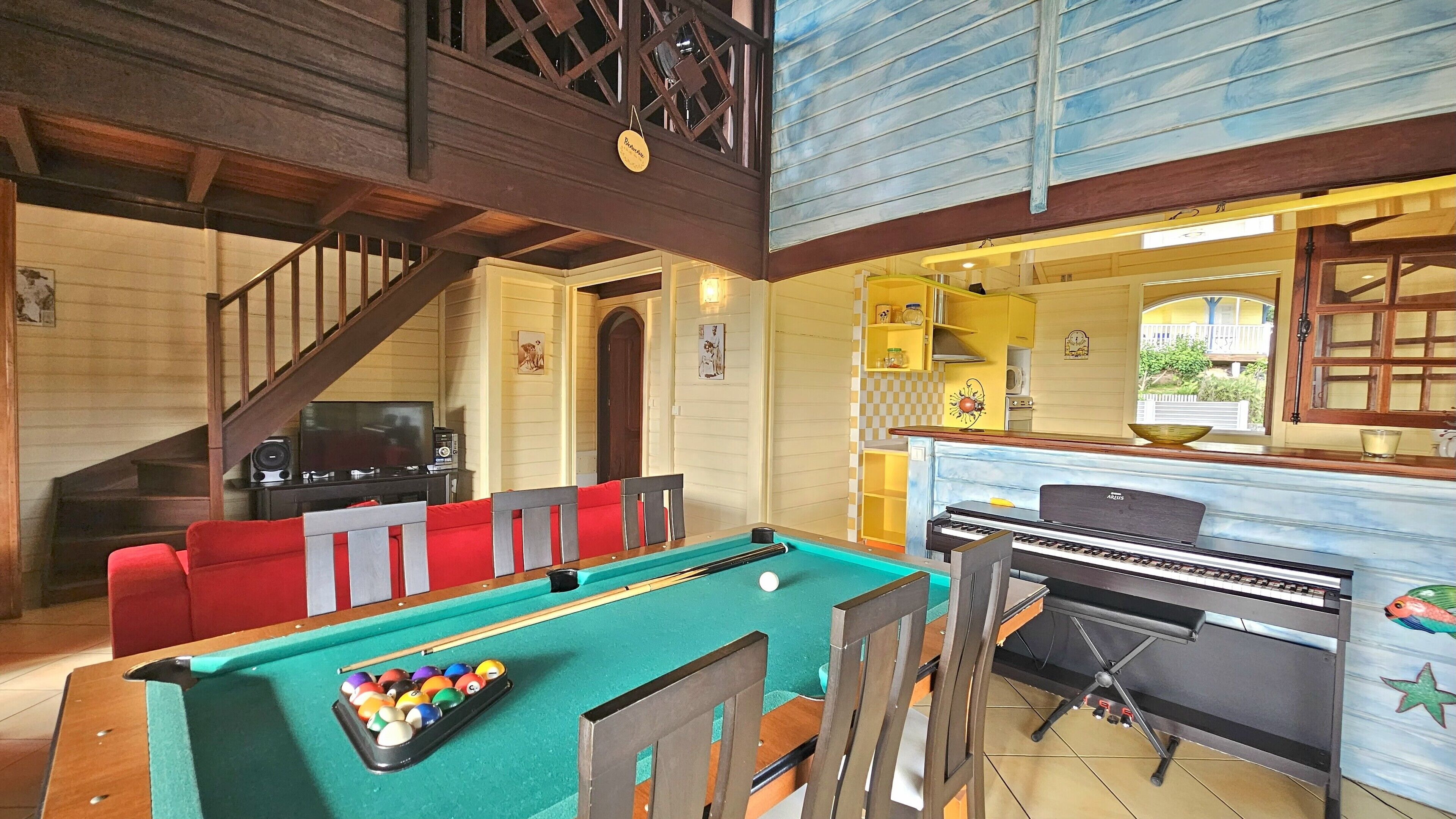 A pool table with a pool cue and balls, a piano, and a dining area with red chairs.