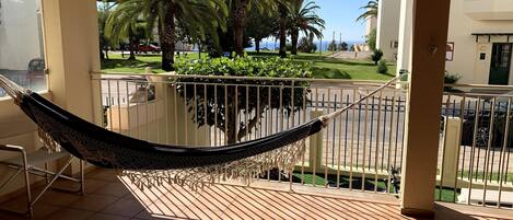 A hammock on a balcony with a view of palm trees and a street.