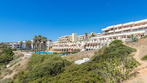 Un hôtel situé sur la côte, doté de nombreux balcons, d’une piscine et d’une végétation luxuriante.